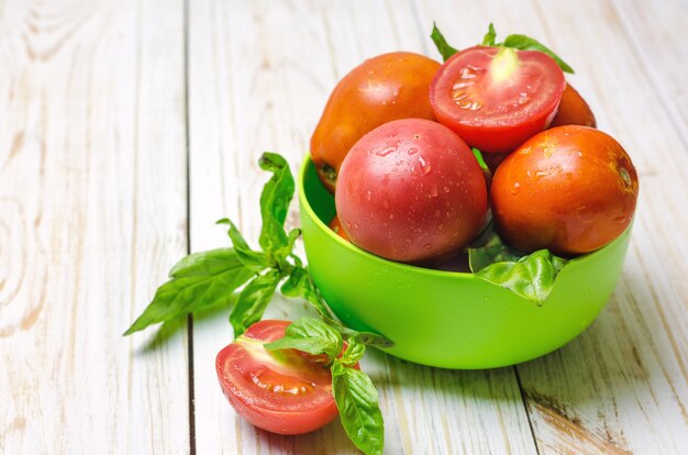 Tomates maduros naturales y albahaca en un tazón verde.