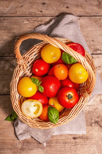 Tomates maduros surtidos con albahaca fresca. Verduras de nueva cosecha en una canasta de mimbre. Fondo de madera vieja, vista superior