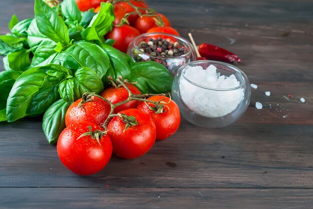 Tomates y manojo de albahaca verde fresca en un fondo de madera oscuro