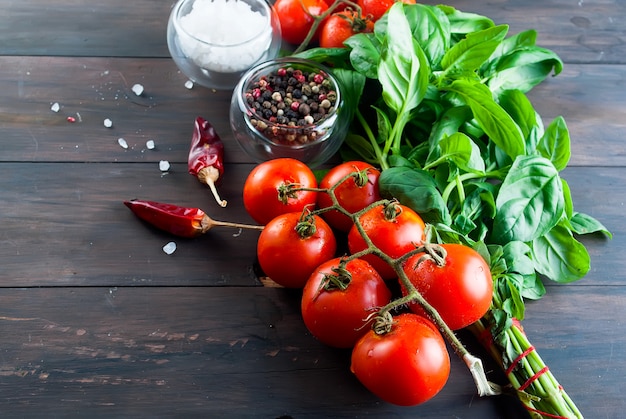 Tomates y manojo de albahaca verde fresca en un fondo de madera oscuro