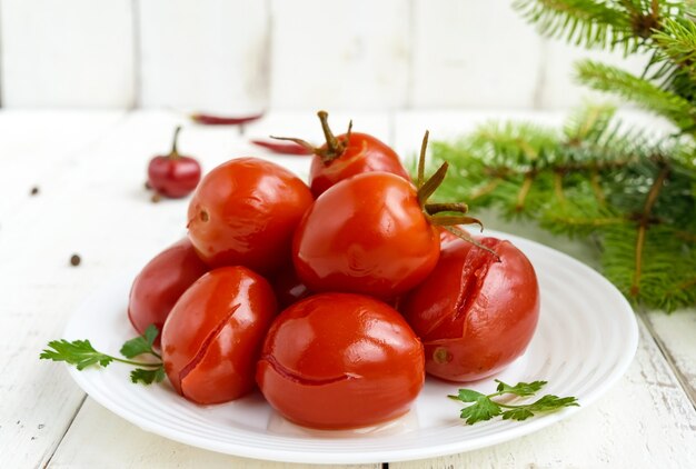 Tomates marinados picantes jugosos en un plato blanco. Sobre un fondo claro, vista superior.