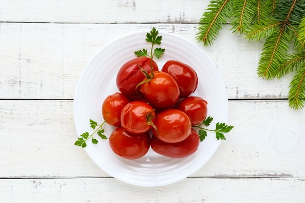 Tomates marinados picantes jugosos en un plato blanco, vista superior.