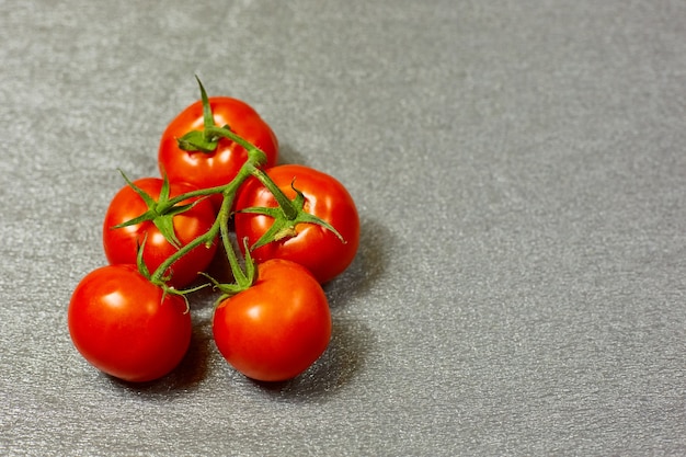 Tomates orgânicos vermelhos em um galho verde em um fundo cinza