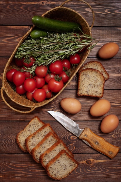 Tomates, pepinos, alguns raminhos de ovos de galinha com alecrim e pão fatiado em uma mesa de madeira