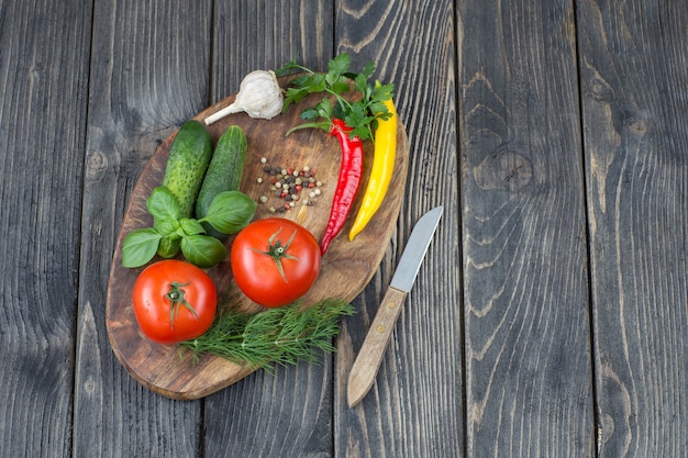 tomates, pepinos, especias, hierbas y cuchillo en una tabla de madera