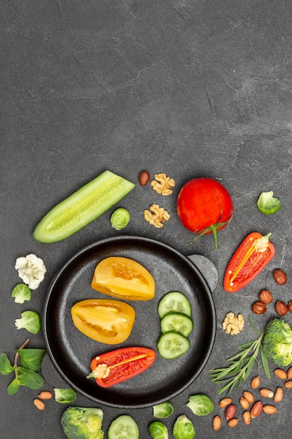 Tomates, pepinos y pimientos picados en una sartén. Verduras y frutos secos en la mesa. Fondo negro. Endecha plana. Copia espacio