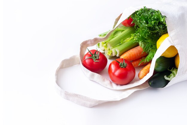 Tomates, pepinos, zanahorias, apio, lechuga verde y limón en una bolsa de lino reutilizable ecológica natural de tela aislada sobre una superficie blanca
