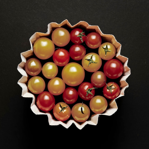 Los tomates pequeños de cereza son amarillos y rojos en un recipiente de papel Tomates pequeños sobre un fondo negro