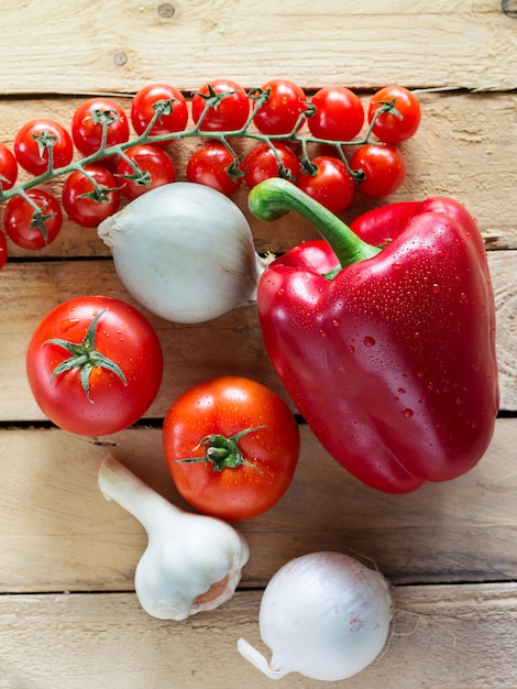 Foto tomates, pimientos, cebollas y ajos sobre una superficie de madera