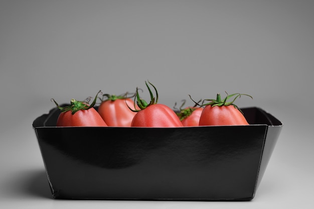 Tomates en un recipiente de papel Tomates frescos en caja sobre fondo negro