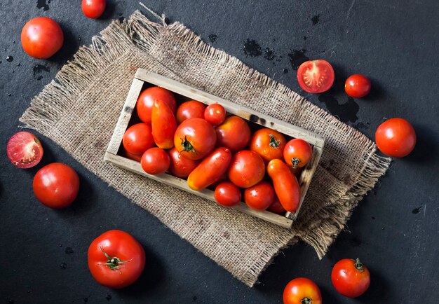 Tomates rojos frescos en caja de madera sobre fondo negro. Endecha plana, vista superior