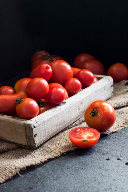 Tomates rojos frescos en caja de madera sobre fondo negro.