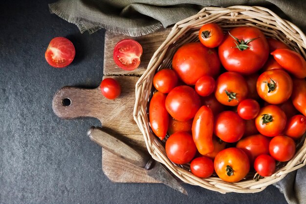 Tomates rojos frescos en canasta de mimbre sobre fondo negro. Endecha plana, vista superior