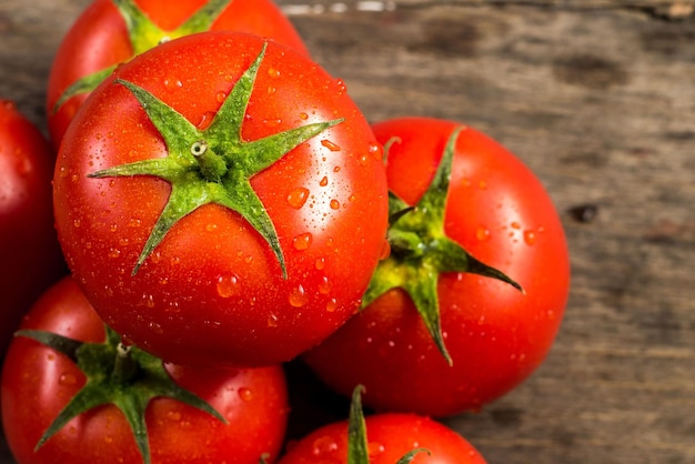 Tomates rojos frescos con gotas de agua sobre fondo de madera