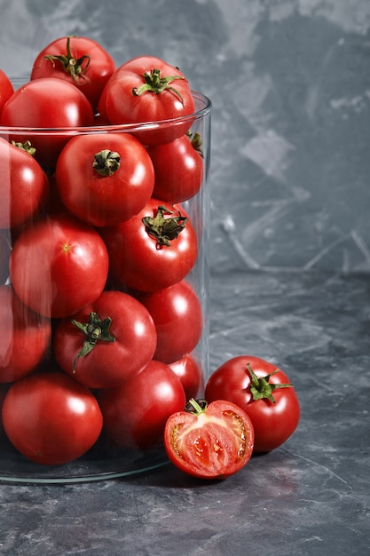 Tomates rojos medianos con un jarrón de vidrio sobre un fondo gris