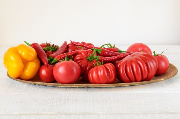 Tomates rojos pimiento rojo y pimentón amarillo en plato sobre mesa blanca