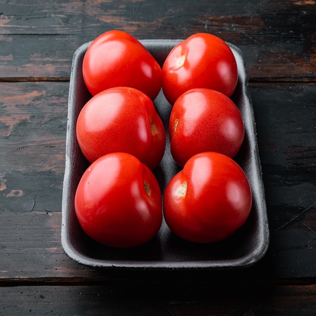 Tomates rojos, sobre mesa de madera oscura.