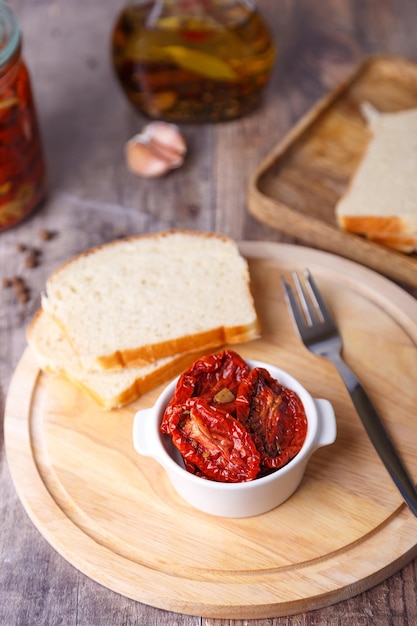 Tomates secos en aceite de oliva en una tabla redonda con pan casero en un estilo rústico Cocina casera tradicional Primer plano de enfoque selectivo