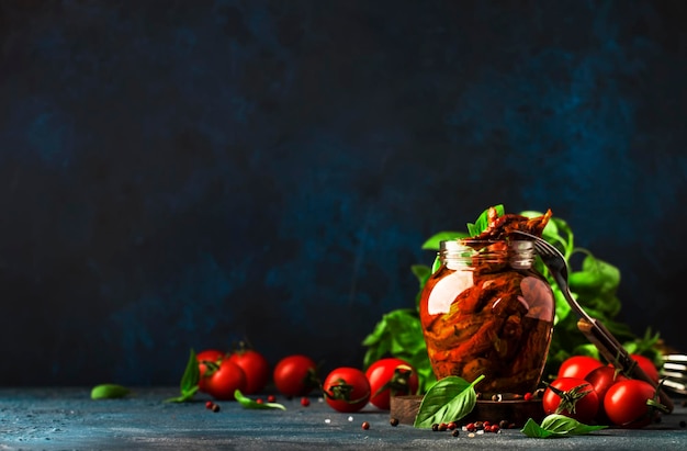 Tomates secos ao sol italianos em azeite com manjericão verde e especiarias em frasco de vidro no espaço de cópia da mesa de cozinha azul