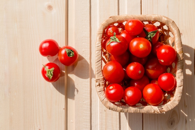 Tomates, tomate cherry en la canasta sobre mesa de madera.