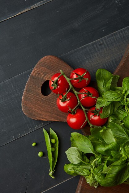 Tomates uva frescos con albahaca y judías verdes para usar como ingredientes de cocina en la tabla de madera sobre un fondo oscuro con copyspace