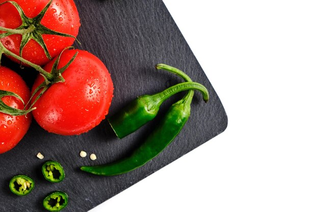 Tomates y vaina de pimiento picante en la placa de corte de pizarra aislado fondo blanco.