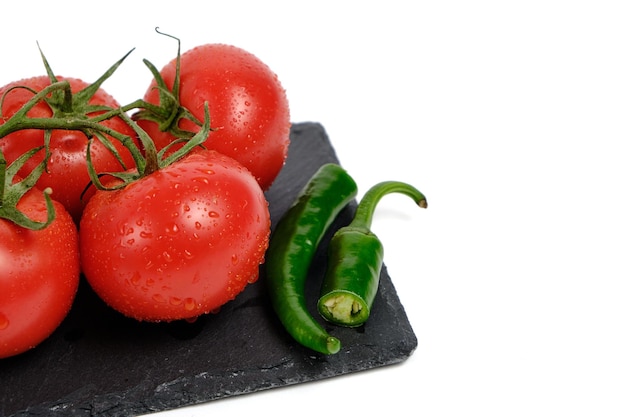 Tomates y vaina de pimiento picante en la placa de corte de pizarra aislado fondo blanco.