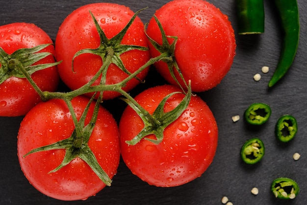 Tomates y vaina de pimiento picante en placa de corte de pizarra