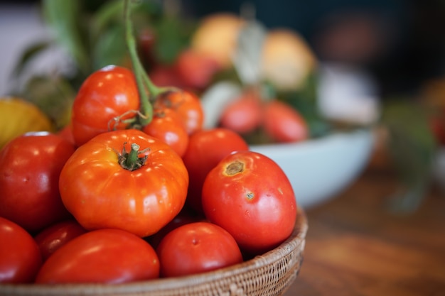 Tomates vermelhos crus frescos em uma cesta na mesa de madeira