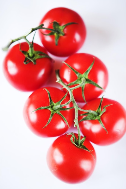 Tomates vermelhos em um galho verde sobre fundo branco