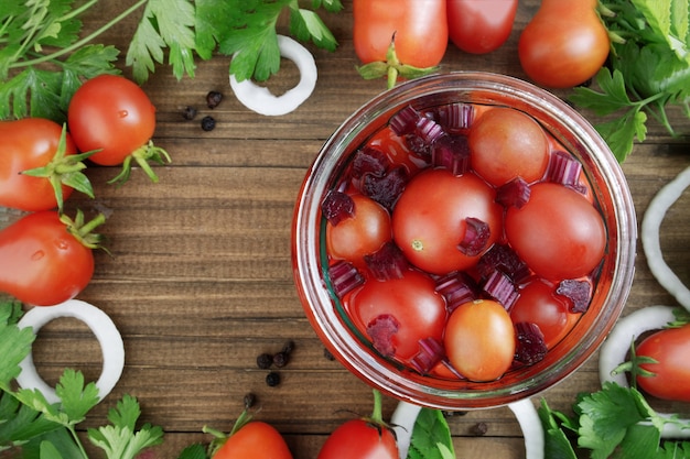 tomates vermelhos em uma jarra em um fundo de madeira com tomates, folhas e cebola