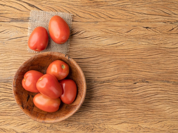 Tomates vermelhos em uma tigela sobre mesa de madeira com espaço de cópia