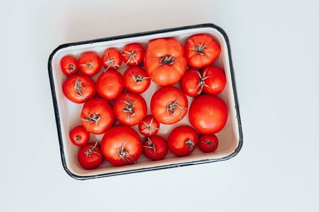 Tomates vermelhos frescos de tamanhos diferentes em uma tigela de esmalte sobre a mesa