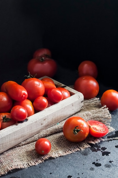 Tomates vermelhos frescos em caixa de madeira em fundo preto.