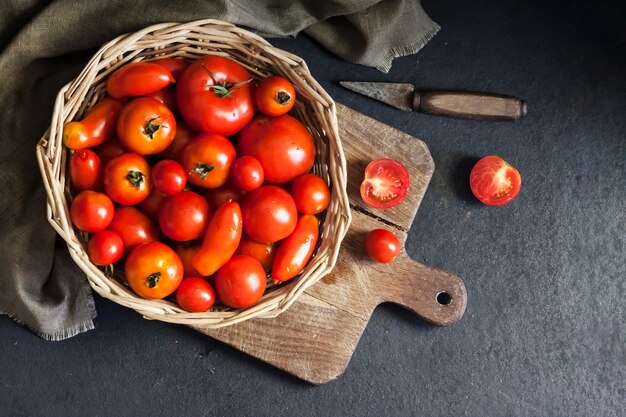 Tomates vermelhos frescos em uma cesta de whicker em fundo preto. Camada plana, vista superior