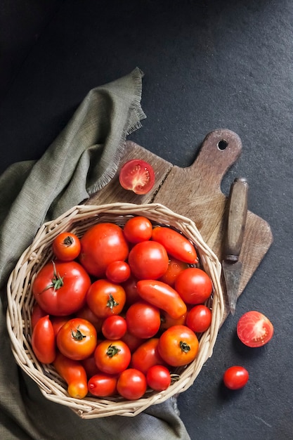 Tomates vermelhos frescos em uma cesta de whicker em fundo preto. Camada plana, vista superior