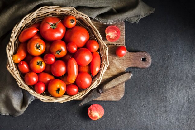 Tomates vermelhos frescos em uma cesta de whicker em fundo preto Espaço de cópia de vista plana de cima