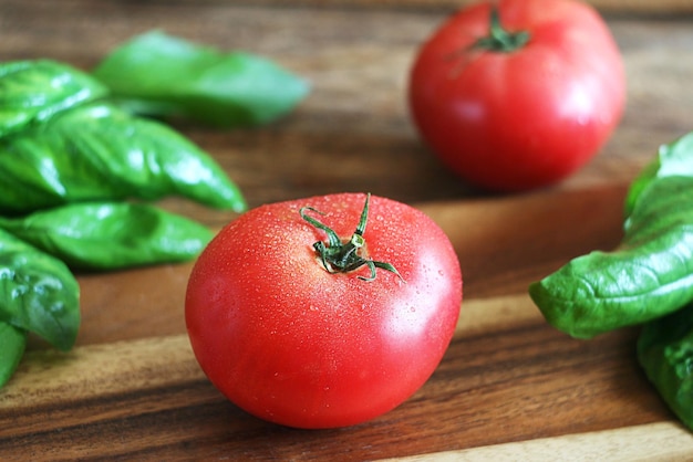 Tomates vermelhos lavados estão em uma placa de madeira, o manjericão está nas proximidades