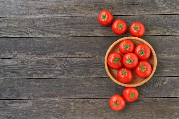 Tomates vermelhos orgânicos em uma tigela de madeira sobre uma mesa de madeira rústica com espaço de cópia para o texto.