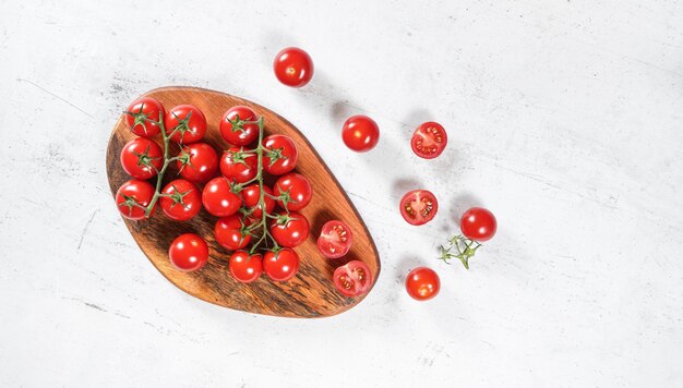 Foto tomates vermelhos pequenos e vibrantes com videiras verdes em tábua de corte de madeira mesa de pedra branca sob a vista de cima