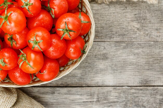 Tomates vermelhos pequenos em uma cesta de vime em uma tabela de madeira velha. Cereja madura e suculenta