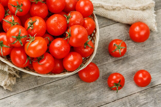 Tomates vermelhos pequenos em uma cesta de vime em uma tabela de madeira velha. Cereja madura e suculenta