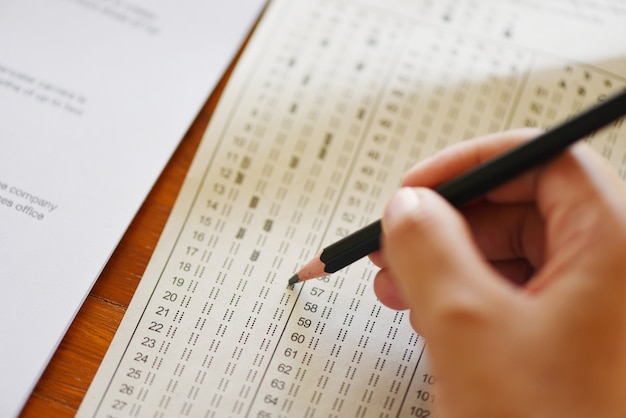 Tome el examen final estudiante de secundaria con lápiz escrito en hoja de respuestas en papel.