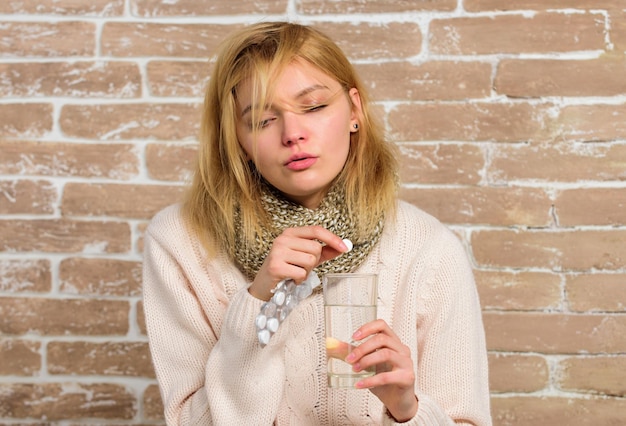 Tome medicamentos para reducir la fiebre. Mujer, bufanda de pelo despeinado, sostenga agua de vidrio y ampollas de tabletas. La niña se siente enferma, tiene fiebre y toma medicamentos. Remedios para el dolor de cabeza y la fiebre.