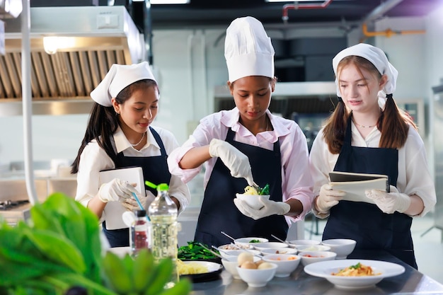 Tome nota en el libro Clase de cocina grupo de aulas culinarias de jóvenes estudiantes multiétnicas felices que se centran en lecciones de cocina en una escuela de cocina