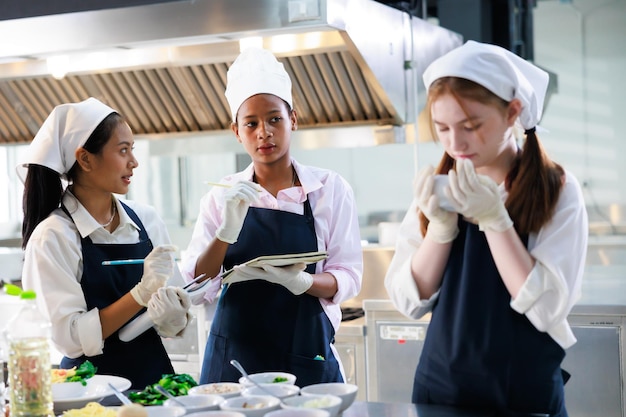 Tome nota en el libro Clase de cocina grupo de aulas culinarias de jóvenes estudiantes multiétnicas felices que se centran en lecciones de cocina en una escuela de cocina