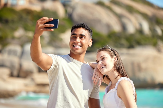 Tome una selfie para capturar este momento para siempre Foto de una pareja joven tomando selfies en la playa