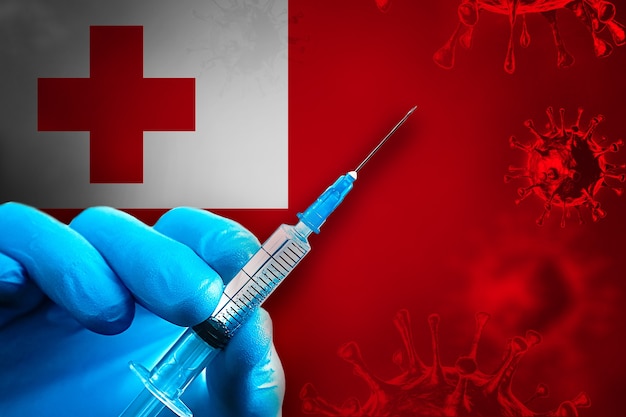Tonga Campaña de vacunación Covid19 Mano en un guante de goma azul sostiene la jeringa delante de la bandera