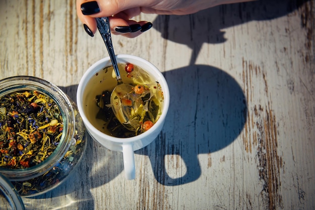 Toning Morgentee gibt einen fröhlichen Start in den Tag Gebrühter Tee in einer Tasse auf Holztisch Womans Hand hält einen Teelöffel Kräutergetränke für Gesundheit und Schönheit