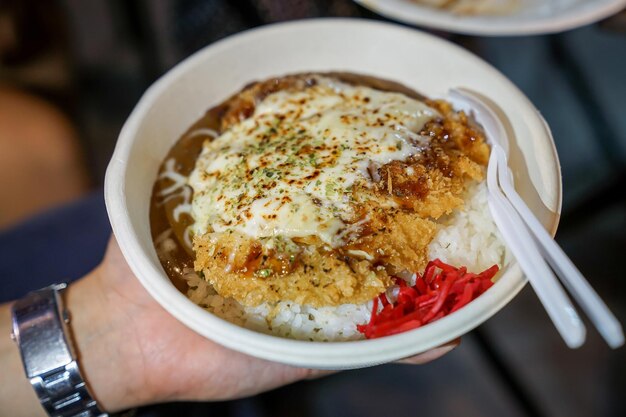 Tonkatsu; traditionelles japanisches Essen, knusprig gebratenes Schweinefleisch mit Saucen oben und Reis darunter, in der Papierschale. Lebensmittelstraße von Bangkok, Thailand.